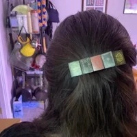 Detailed view of colorful miniature book stack hair clip worn on long brunette hair