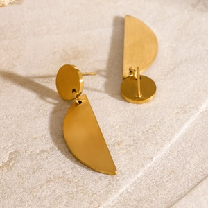 Detail of gold brushed stainless steel earrings on stone surface with long shadows