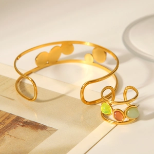 Detailed shot of open gold bracelet and three-color natural stone ring on warm backdrop