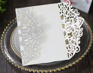 Detailed view of laser-cut white wedding invitation with silver glitter on a glass plate