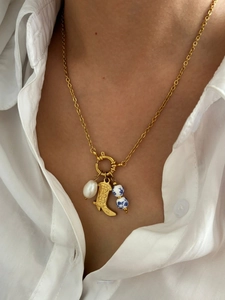 Close-up of golden necklace with cowboy boot pendant, baroque pearl and blue porcelain beads