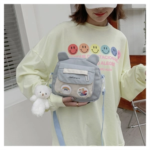 Detail of grey canvas crossbody bag with cute teddy bear charm and rainbow patch