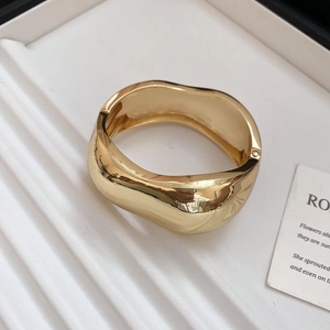 Detail view of the wide gold irregular wave bangle with high-polished mirror finish