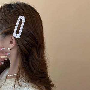 Close-up of white rectangular hair clip with black stitching detail on brown hair