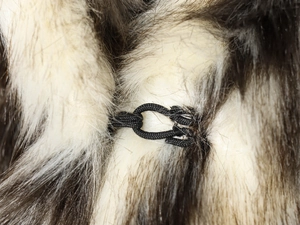 Close-up of beige faux fur coat texture with black braided cord fastener detail