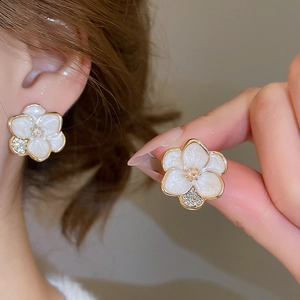 Close-up of white enamel flower earring with gold edges and sparkling micro-inlaid zircons