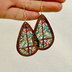 Close-up of teardrop earrings featuring stained glass church patterns and wooden frames