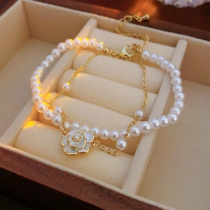 Detail of camellia flower charm and white pearls on a gold-plated layered bracelet