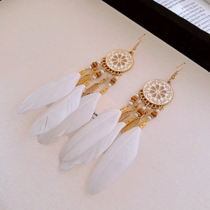 Détail de boucles d'oreilles bohèmes avec disques en alliage, perles en bois et plumes