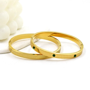 Detail of gold titanium steel bangle with green zircon stone and textured scale pattern