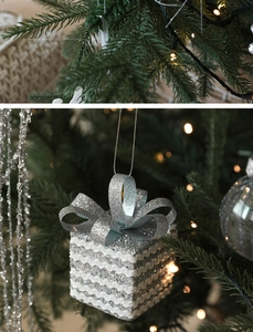 Close-up of silver glitter gift box ornament with bow on Christmas tree branch