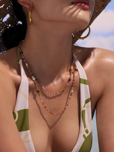 Close-up of colorful beaded double-layer necklace and golden hoop earrings on model at beach