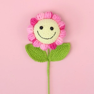 Gros plan d'un tournesol au crochet rose et jaune avec un visage souriant sur fond rose