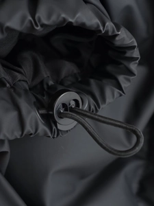 Detail of adjustable drawstring toggle on black matte tech fabric puffer vest