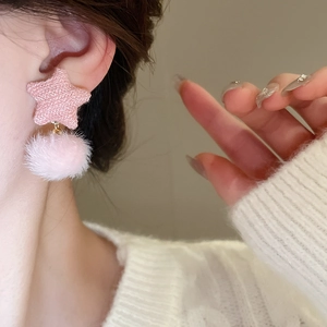 Nahaufnahme von rosa Stern-Ohrringen mit Plüschkugeln an einem Modell im weißen Strickpullover