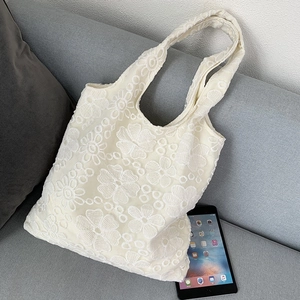 Detail view of beige lace tote bag with floral embroidery next to a tablet on a sofa