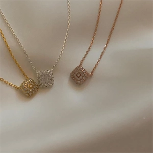 Close-up of square zircon pendants in gold, silver, and rose gold on white fabric