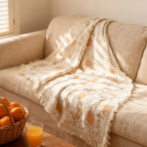 Floral printed cotton muslin baby swaddle blanket with tassels on a cozy beige sofa