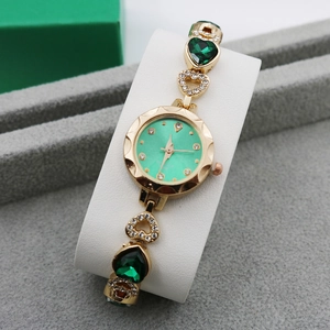 Detail of rose gold bracelet watch featuring green heart crystals and inlaid diamonds