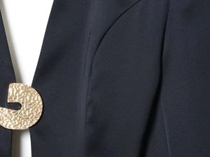 Gros plan d'un bouton doré martelé sur une robe courte bleu marine au tissu texturé