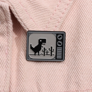 Macro di una spilla in smalto a forma di TV pixel con dinosauro su denim rosa