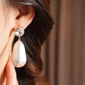 Gros plan sur des boucles d'oreilles dorées avec zircon rond et perle blanche en goutte