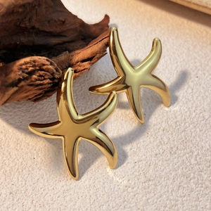 Polished 18k gold plated stainless steel starfish stud earrings on natural wood decor