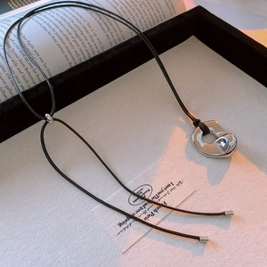 Detailed macro of a fluid organic metal pendant on a minimalist black cord necklace