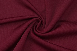 Macro shot of dark red knitted fabric texture with elegant swirl pleats and stitching
