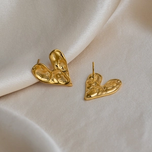 Vue macro de boucles d'oreilles cœur en or 18K avec texture lave sur du tissu satiné