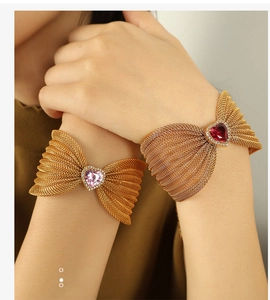 Detail of gold mesh bow bracelet featuring heart-shaped pink gem with micro-pave diamonds