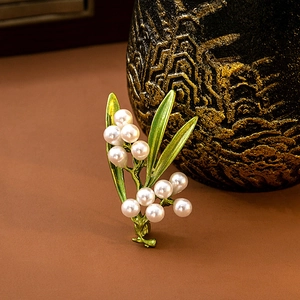 Macro detail of leaf-shaped brooch with green enamel leaves and white pearls