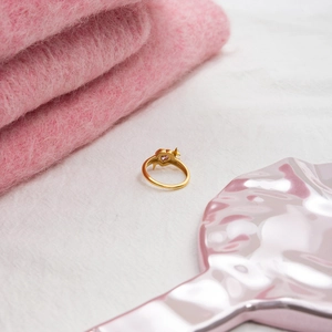 Detail of pink heart zircon and star gold ring on elegant soft white and pink fabrics