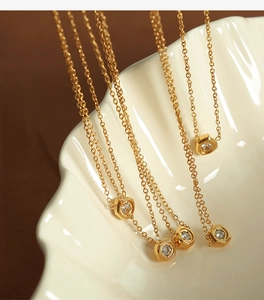 Detail of hexagon pendants with zircons on gold necklaces draped over a shell tray