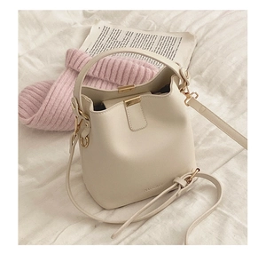 Close-up of beige PU leather bucket bag with gold hardware and brand logo on a bed