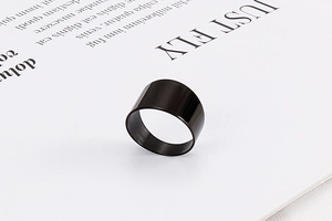 Close-up of a wide black titanium steel band ring on minimalist paper background