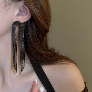 Detail of long U-shaped black tassel earrings with rhinestones worn by a model