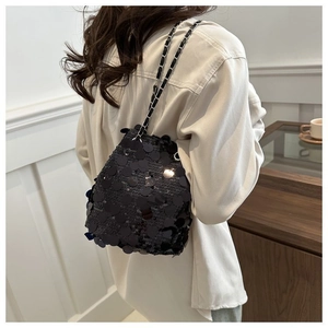 Detail of black sequin bucket bag with silver chain strap shown on a female model