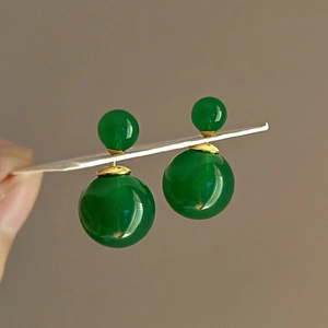 Close-up of green double-bead stud earrings with gold finish and smooth polished texture