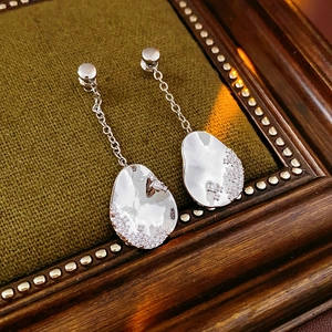 Détails de boucles d'oreilles asymétriques argentées en goutte avec cristaux sur tissu vert