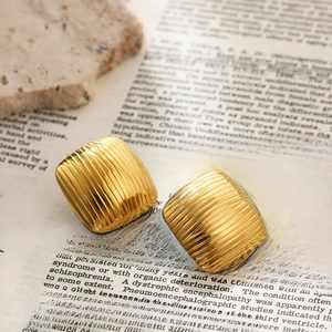 Macro detail of square gold-plated earrings featuring elegant vertical stripe textures