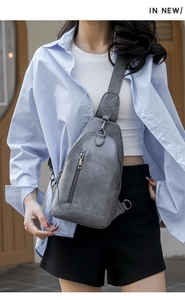 Sac bandoulière en similicuir gris mat avec poche zippée, porté par un mannequin en style décontracté