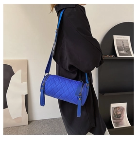 Close-up of quilted blue cylinder shoulder bag worn by model in a minimalist studio setting