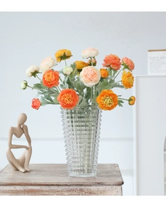 Detail of orange faux ranunculus flowers in a textured geometric glass vase