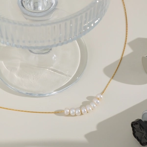 Elegant gold chain necklace featuring seven natural white pearls on a minimalist background