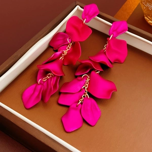 Détail de boucles d'oreilles pétales magenta avec chaîne dorée dans une boîte cadeau