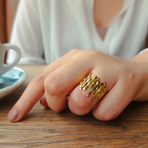 Close-up of golden irregular lava texture ring worn by model in a cozy cafe setting