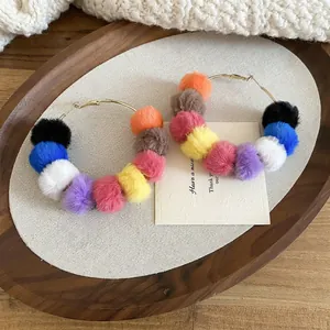 Golden round hoop earrings with colorful plush pom-poms shown on a wooden tray
