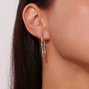 Close-up of a silver wave-shaped earring worn by a model, showing sleek metallic texture