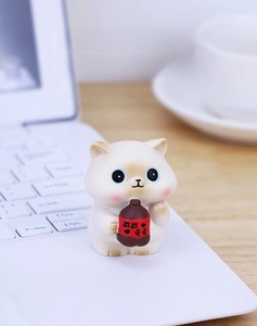 Close-up of a cute white cat figurine holding a small brown bottle on a wooden office desk